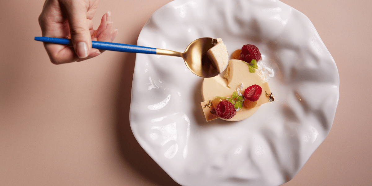 Hand delicately picking up panna cotta with a blue and gold spoon.