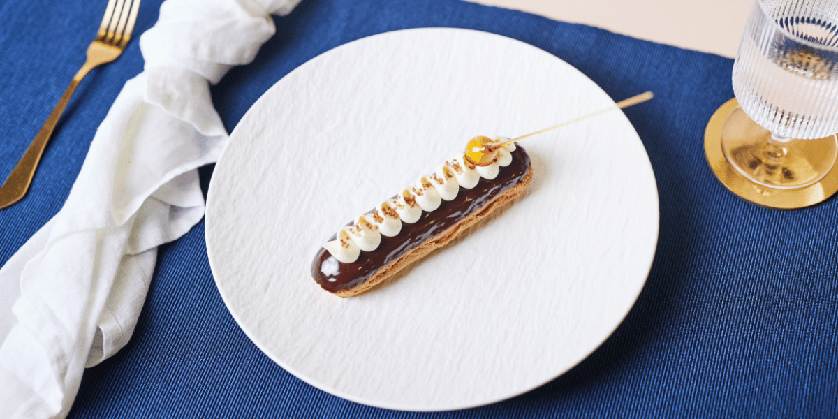 Eclair au chocolat on white plate atop navy placemat.