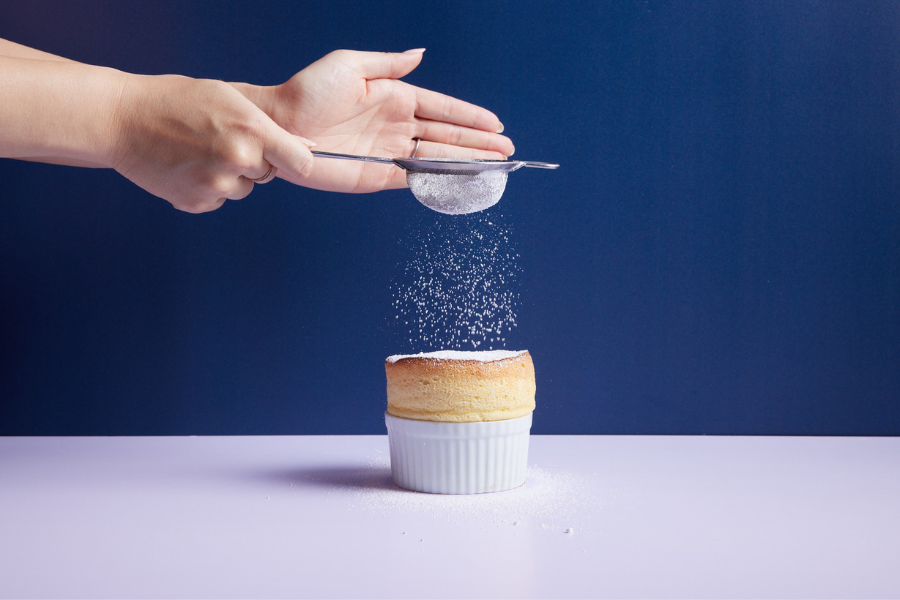 Hand dusting icing sugar over freshly cooked souffle