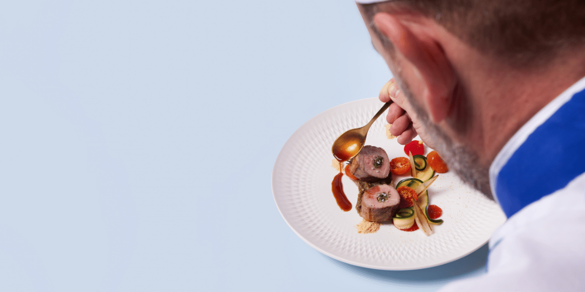 Chef plating up dish on blue backdrop